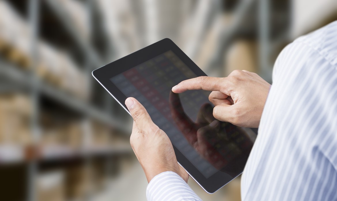 Person reviewing inventory on a tablet in a warehouse storage aisle. Person reviewing inventory on a tablet in a warehouse storage aisle.
