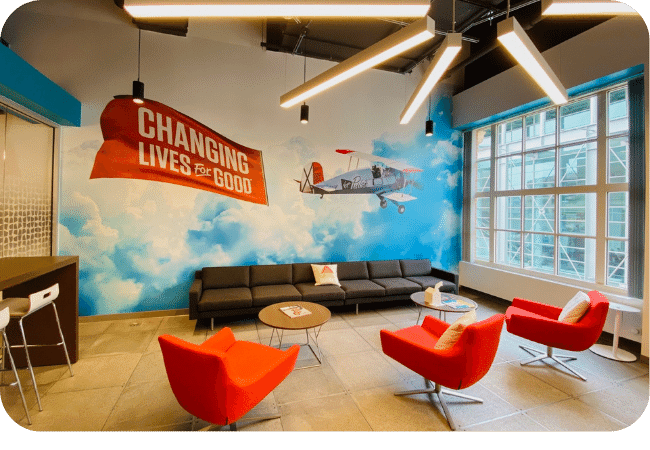 A modern lounge area featuring a mural and bright red chairs.