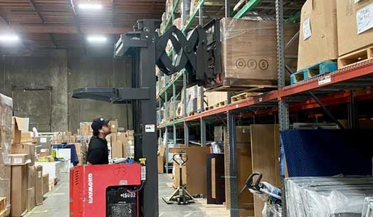 A warehouse interior with tall storage racks, boxed inventory, and a person operating a forklift.