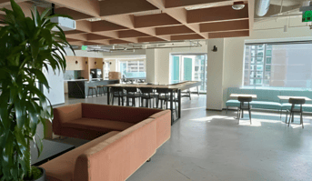 A modern office space with terracotta sofa, large windows, and open-plan area.