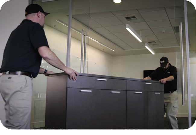 Two people moving a large filing cabinet in an office setting.