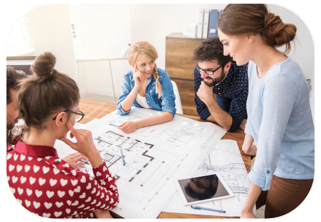 A group of coworkers collaborating around a table, reviewing architectural plans and designs using laptops and digital tablets.