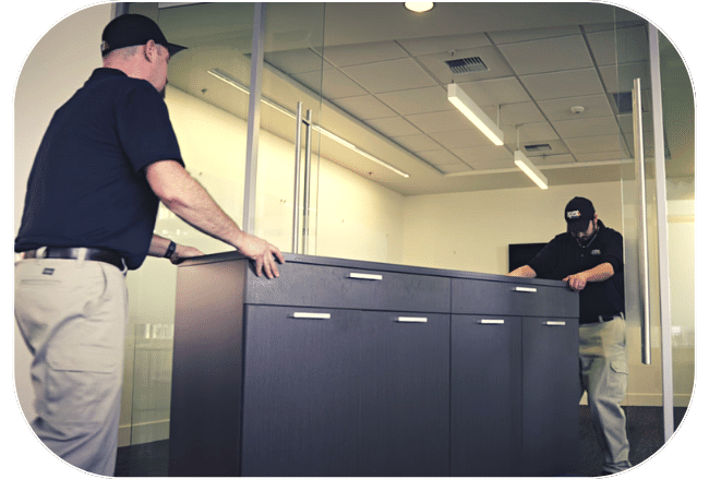 Two people moving a large filing cabinet in an office setting.