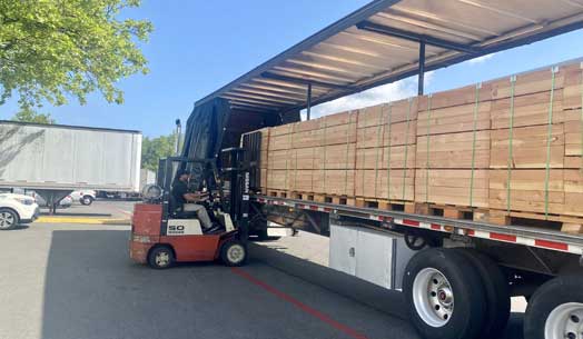 Forklift loading wooden crates onto a semi-truck outdoors.