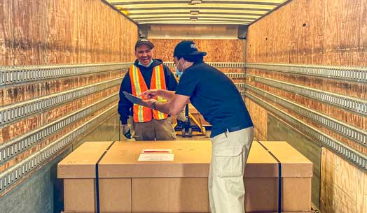 Two workers loading boxed cargo inside a truck trailer.
