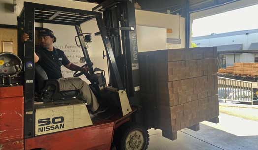 Forklift operator moving a large wooden crate in a warehouse.
