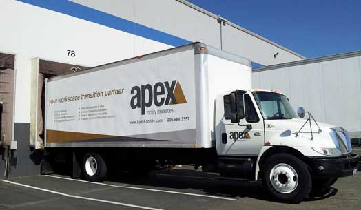 White Apex delivery truck parked outside a warehouse.