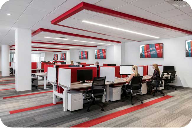 Modern red and white office space with employees working at computer stations.