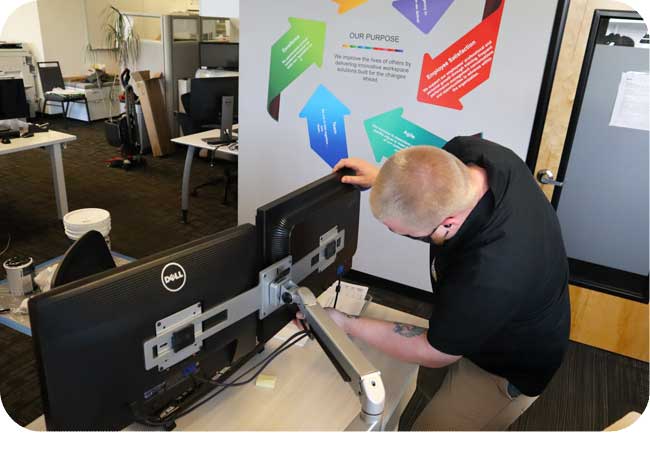 Technician installing dual monitors near a colorful company values display.