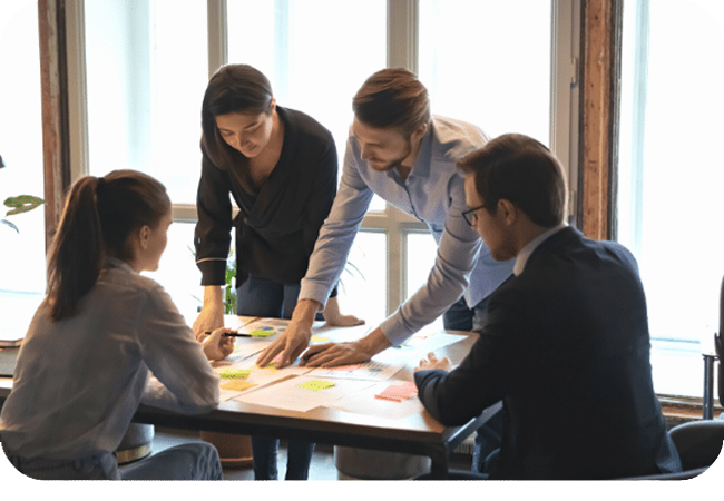A group of five coworkers collaborate around a table, reviewing documents.