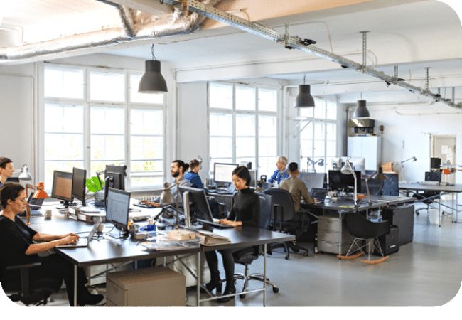 An open office space with multiple people working at desks and computers.