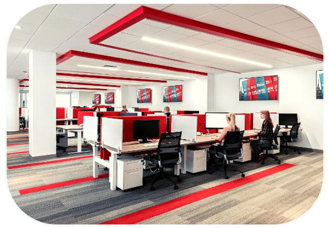 An open-plan office space with rows of desks, computers, and people working at their stations. 