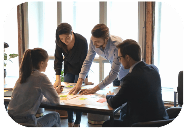 A group of five coworkers collaborate around a table, reviewing documents.