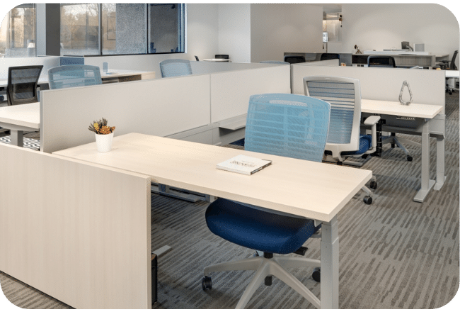 An open office space with white cubicles, light wood desks, and blue chairs.